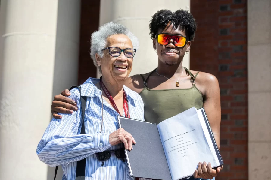 “In many ways, my honors thesis has been a source of love, for which I will forever be grateful.”

A crowd of about 50 students, faculty, and staff gathered on the front steps of Coram Library to celebrate Sam Jean-Francois ’23 of Medford, Mass., and bind Jean-Francois’ honors thesis in Africana, titled “Colonialism as the Disaster: Retelling the Fight for Haitian Sovereignty,” with Associate Professor and Co-Chair of Africana Sue Houchins serving as Jean-Francois’ “proud adviser.”

The thesis “has been a heuristic exercise centered in my journey to uncover more about my history, my family’s history, and Haiti’s history as the world’s first free Black republic,” said Jean-Francois.

“Through this thesis I’ve had the opportunity to engage with the works of Haitian scholars such as Myriam Chancy, and reconnect with my mother tongue, Kreyol.”

Laughing at calls to read the whole thesis aloud (all 126 pages of it,) Jean-Francois read the acknowledgments page aloud, and then bound the thesis, with the help of Verina Chatata ’26 of Lilongwe, Malawi, followed by a joyous shake-and-pop with a bottle of champagne, adorned with a Haitian flag.