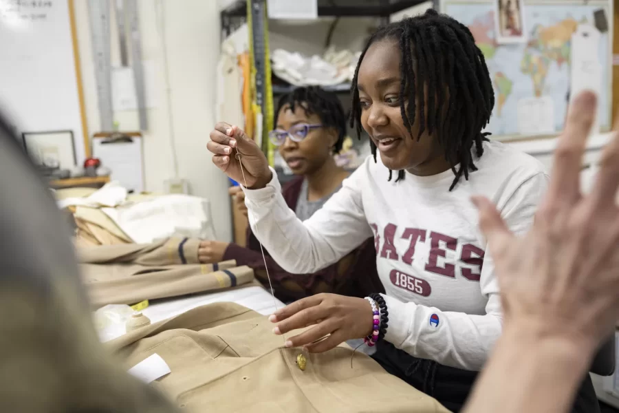 Stepping into the costume shop in Schaffer Theatre is like entering a whole new world, tucked under the stairs: colorful fabrics cover the walls, along with photos of costumes from past productions, spools of colored thread are impaled on a rack on the wall, and in the back, guarded by a small army of mannequins, racks and racks of costumes hang waiting to be worn.

It’s 2:20 in the afternoon, and Carol Farrell, the costume shop supervisor, is taking a tea break with two of her student workers, Bora Lagunda ’25 (in white Bates sweatshirt) of Kinshasa, Congo and Lauren Reed ’23  (in gray and garnet top) of Baton Rouge, La.

Also stopping by for measurements (and to try on a rain hat and rain boots — they were a bit big for him, so maybe they will stuff them with socks) was Brendan Fitzgerald ’23 of New Rochelle, N.Y., whose character “The Watchman” is one of the Bar Harbor locals in Tim Dugan’s production of Shakespeare’s “Much Ado About Nothing,”  Senior Lecturer in Theater and Managing Director of Theater and Dance Michael Reidy also dropped in for a conversation with Lauren Reed.