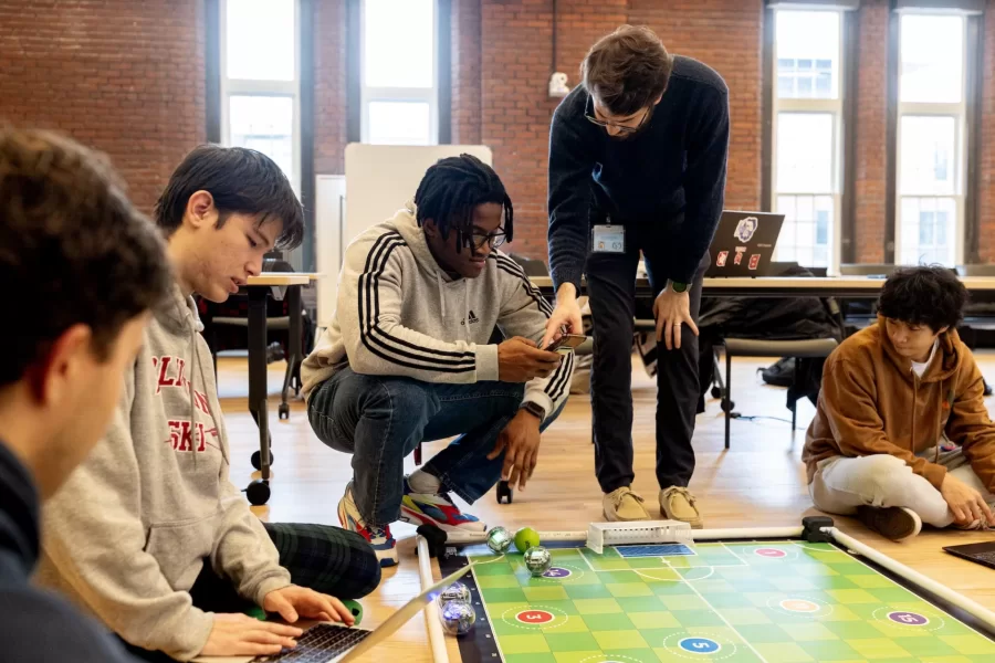 Small, but sophisticated.

That’s what first-year students of Professor of Mathematics Meredith Greer discovered about one kind of small robot during a visit to Bates by a team of Lewiston Public Schools educators on Nov. 14.

The team of instructional specialists and tech coaches brought Sphero BOLT robots with them during the morning visit to Chase Hall Lounge. Designed for educational and recreational purposes, they’re often used in schools to teach coding and robotics.

From left, first-year students Darien Chiang of Quincy, Mass., Julian Tilney of Arlington, Mass., and Finn Sheehy of Burlingame, Calif., get a handle on how to program the robots.

The students are in Greer’s First-Year Seminar, “Learning Math Using Crafts, Coding, and Games,” which investigates “how humans think about math at age 5, age 12, or age 18 and beyond.” During the semester, the students focused on learning through a variety of methods, including hands-on crafts, open-ended class meetings, and age-appropriate computer coding.

This was the educators’ third visit to the course, and for each visit, they brought with them age-appropriate robots.

Connecting with the Lewiston educators, and gaining insights into “specific activities they do with the robots at specific grade levels,” Greer explains, “has given us multiple chances to connect our studies with specific grade-level-based math learning standards that are used across the state of Maine.”

For the Lewiston educators, the three visits reflect growing outreach efforts into their community. “They were both enthusiastic and generous about bringing these lessons into our classroom,” says Greer. “Moving forward, we are continuing to think about ongoing collaborations.”