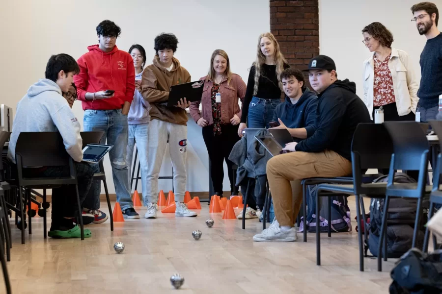 Small, but sophisticated.

That’s what first-year students of Professor of Mathematics Meredith Greer discovered about one kind of small robot during a visit to Bates by a team of Lewiston Public Schools educators on Nov. 14.

The team of instructional specialists and tech coaches brought Sphero BOLT robots with them during the morning visit to Chase Hall Lounge. Designed for educational and recreational purposes, they’re often used in schools to teach coding and robotics.

From left, first-year students Darien Chiang of Quincy, Mass., Julian Tilney of Arlington, Mass., and Finn Sheehy of Burlingame, Calif., get a handle on how to program the robots.

The students are in Greer’s First-Year Seminar, “Learning Math Using Crafts, Coding, and Games,” which investigates “how humans think about math at age 5, age 12, or age 18 and beyond.” During the semester, the students focused on learning through a variety of methods, including hands-on crafts, open-ended class meetings, and age-appropriate computer coding.

This was the educators’ third visit to the course, and for each visit, they brought with them age-appropriate robots.

Connecting with the Lewiston educators, and gaining insights into “specific activities they do with the robots at specific grade levels,” Greer explains, “has given us multiple chances to connect our studies with specific grade-level-based math learning standards that are used across the state of Maine.”

For the Lewiston educators, the three visits reflect growing outreach efforts into their community. “They were both enthusiastic and generous about bringing these lessons into our classroom,” says Greer. “Moving forward, we are continuing to think about ongoing collaborations.”