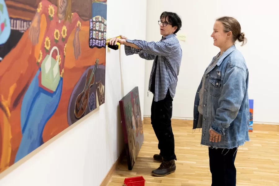 Associate Professor of Art and Visual Culture Carolina González Valencia, adviser in the winter semester to senior studio art majors, install their work in the Bates Museum of Art for the Annual Senior Exhibition on April 9, 2025. On the lower level is Avery Lehman ’25 of Portsmouth, NH, and also exhibition installer…..
Upstaris, González Valencia works with Visiting Lecturer in Art and Visual Culture Michel Droge to help Elizabeth (Lizi)  Barrow ’25 of Winchester, Mass., to hang her painting on the upper level.