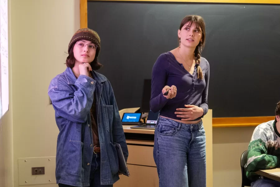Two students glance at the projector screen while giving a presentation to their class.