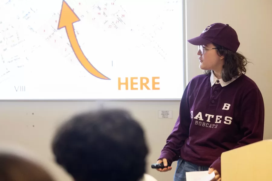 A student glances at the projector screen while giving a presentation to their class.