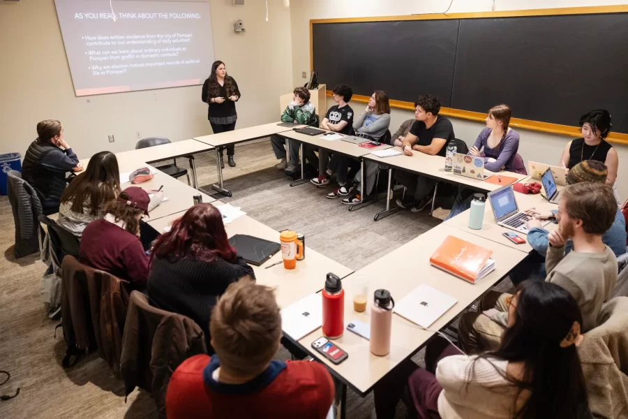 A professor addresses their class sitting in a roundtable-style formation.