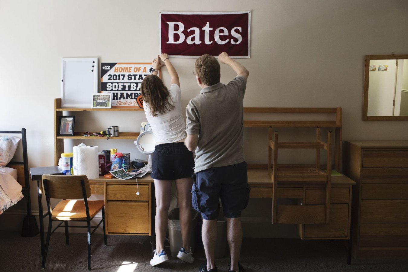 Abra Kaplan '21 of Oak Park, Ill., stretches to pin a Bates College banner on her wall with the assistance of her father Gary Kaplan while moving in to her new dorm at Rand Hall during move in day.