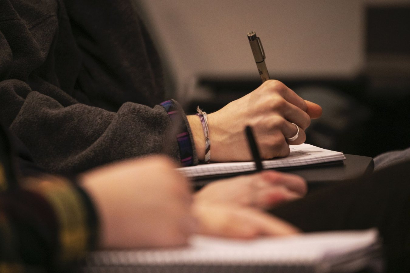 Hand holding a pencil writing in a notebook on a desk