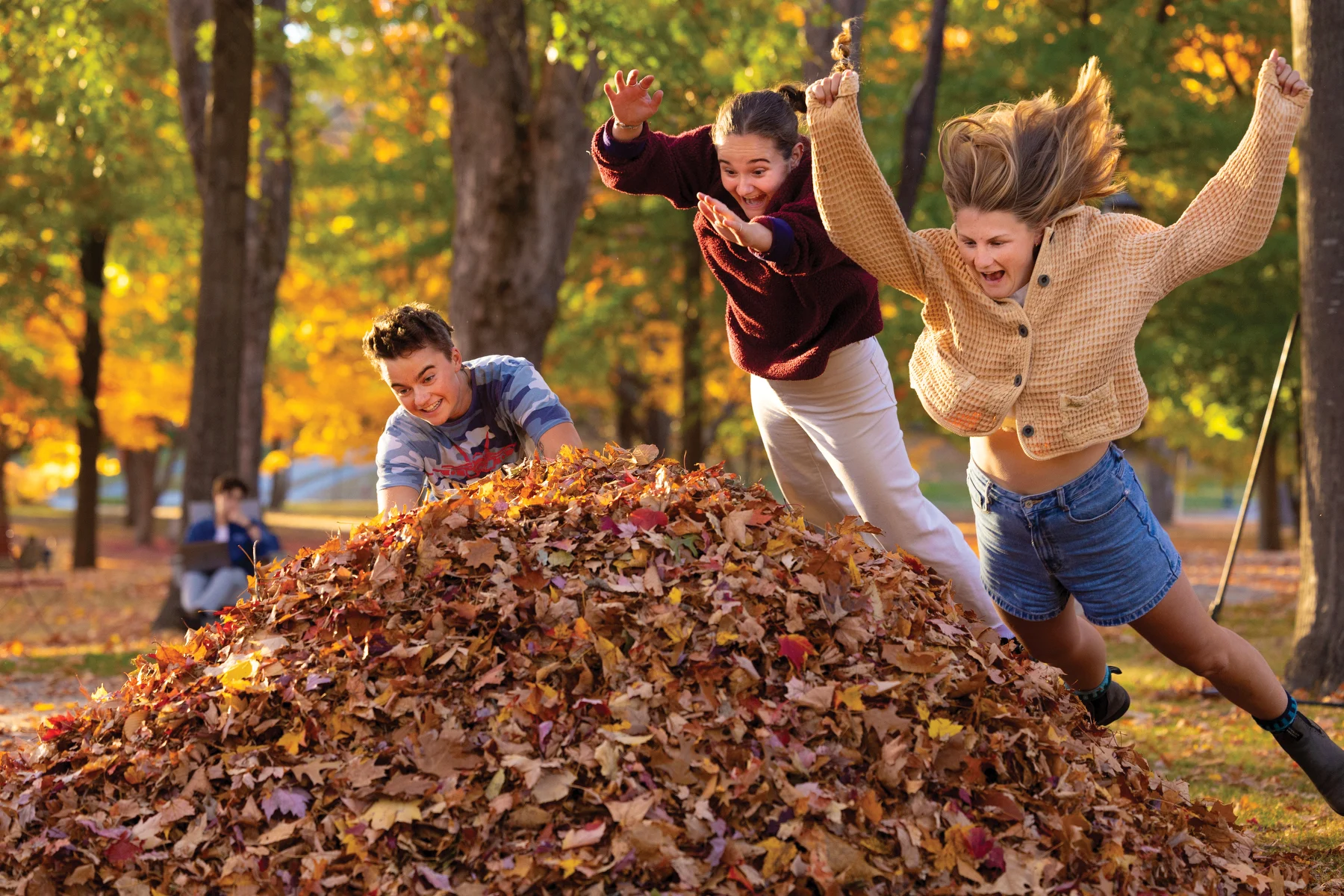 Three students jumping into a leaf pile.