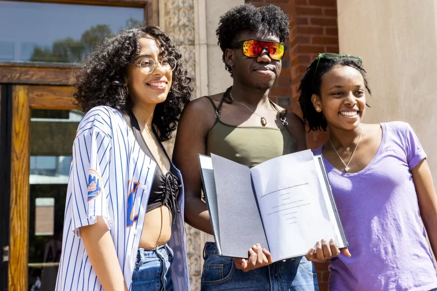“In many ways, my honors thesis has been a source of love, for which I will forever be grateful.”
A crowd of about 50 students, faculty, and staff gathered on the front steps of Coram Library to celebrate Sam Jean-Francois ’23 of Medford, Mass., and bind Jean-Francois’ honors thesis in Africana, titled “Colonialism as the Disaster: Retelling the Fight for Haitian Sovereignty,” with Associate Professor and Co-Chair of Africana Sue Houchins serving as Jean-Francois’ “proud adviser.”
The thesis “has been a heuristic exercise centered in my journey to uncover more about my history, my family’s history, and Haiti’s history as the world’s first free Black republic,” said Jean-Francois.
“Through this thesis I’ve had the opportunity to engage with the works of Haitian scholars such as Myriam Chancy, and reconnect with my mother tongue, Kreyol.”
Laughing at calls to read the whole thesis aloud (all 126 pages of it,) Jean-Francois read the acknowledgments page aloud, and then bound the thesis, with the help of Verina Chatata ’26 of Lilongwe, Malawi, followed by a joyous shake-and-pop with a bottle of champagne, adorned with a Haitian flag.