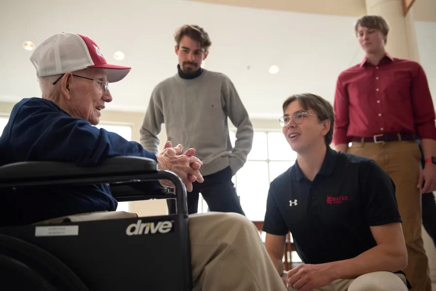 Ralph Sylvester ’50, left, talks with members of the Bates rowing team Aidan Braithwaite ’23 of Milton, Mass.; Isaac Levinger ’24 of Rockville, Md.; and Charles Renvyle ’25 of Hopkinton, N.H. during the dedication of the new rowing shell at Perry Atrium in Pettengill Hall on April 29, 2023.