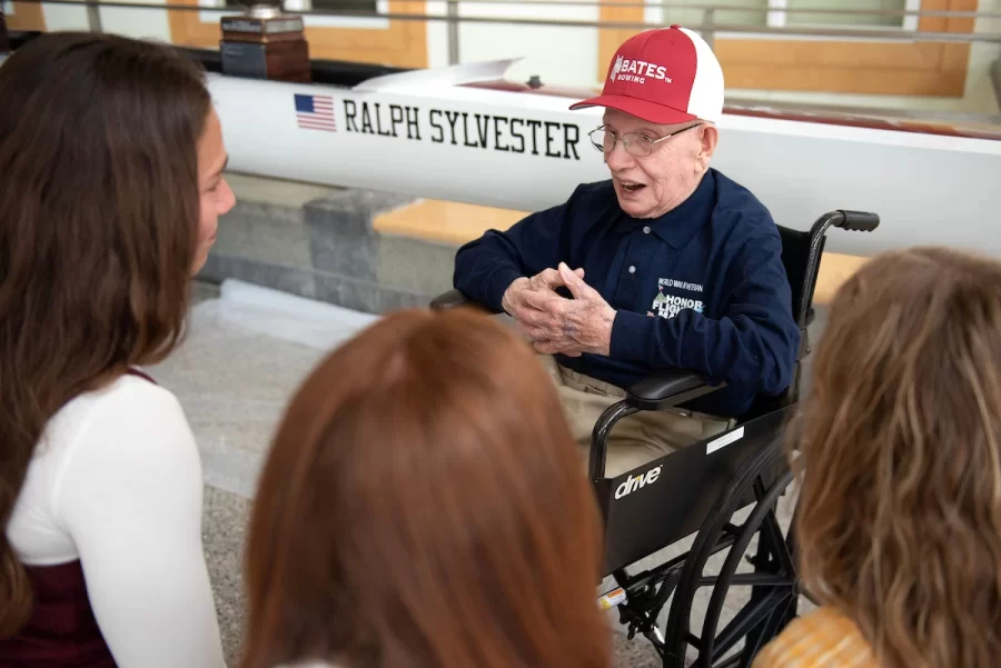 Members of the Bates rowing team from left: Eliana Weissmann ’24 of Newton, Mass.; Katarina Dickson ’24 of Princeton, Mass. and Molly Connors ’23 of Westwood, Mass. talk with Ralph Sylvester ’50 during the dedication of the new rowing shell at Perry Atrium in Pettengill Hall on April 29, 2023.