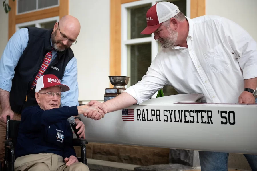 Ralph Sylvester ’50, center, thanks Bates Rowing Head Coach Peter Steenstra, right, after christening the new rowing shell at Perry Atrium in Pettengill Hall on April 29, 2023. Coach Steenstra presented Sylvester with a blade during the dedication ceremony making Sylvester the only non-rower to receive one.