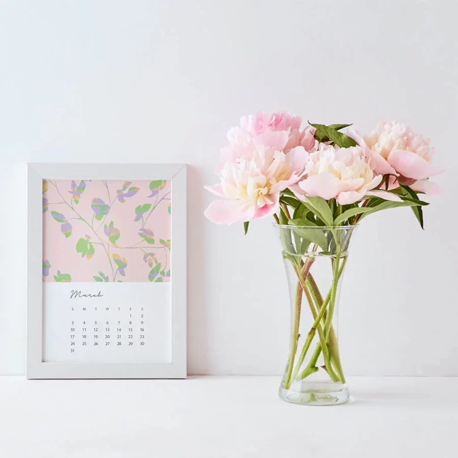 A 5x7 card with the days and dates for March 2024 and a pink floral illustration in a white frame. Next to the fram is a bouquet of pink peonies.