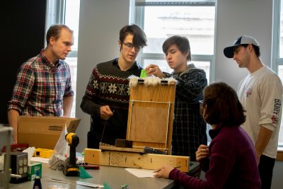 Assistant Professor of Biology Andrew Mountcastle observes as students in his new course on "Bioinspiration and Biomimetics" (from left) Thad Gunther '21, Jeremy Bennett '21, Josh Turner '20, and Ruth van Kampen '19 test the performance of their 3D printed models of grooming brushes that are inspired by cat tongues. Swipe left to see a few scenes from today’s lab.. The exercise was part of a course project motivated by a recent academic paper that discovered that grooming brushes inspired by cat tongues perform better than typical human hairbrushes. Cats use hollow papillae (the grooves in their tongues) to wick saliva into their fur. Student IDs: Erin Murphy '21 in denim jacket Eve Cinquino '19 in black and shite patterned pullover with Andrew Hiram Martin '19 in plaid and Elly Bengtssom '19 in red pullover With raisins: Wendy Memishian '19 in black and plaid and Bridget Tweedie '21 in paisley Gavin Chen '20 side loading scale and Brianna Karboski '21with white and pink pullover at laptop and in background Joseph Ho '20 in blue plaid. Josh Turner '20 with Sea Saba hat and Ruth van Kampen '19 in purple pullover Thad Gunther '21 in grey with snowflakes sweater and glasses with Jeremy Bennett '21 in blue plaid shirt with hood Blonde hair: Abby Hamilton '21 and Julie Hinton ;20 in cowl sweater Alex Bickart '21 tall blond hair pulling cat hair