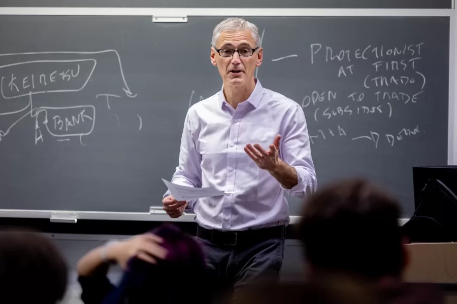 a professor stands in front of a blackboard addressing the class