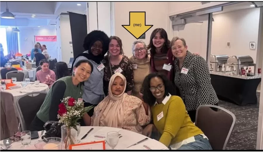 Eight women pictured smiling and arranged in two rows, the first of which has three women seated at a table in and five women standing behind them