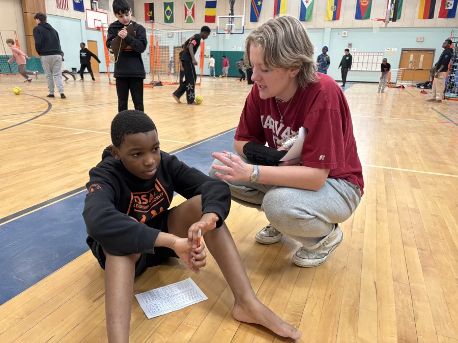A school-aged child sits on the floor looking out to the distance while a Bates student is crouched on the floor to the child's side and facing him seemingly in conversation