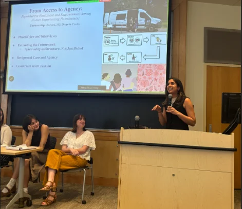 A student at a podium with a slide show projection in the background and seated students in the foreground