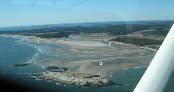 This aerial photograph of Popham Beach on March 10, 2010, shows key elements of erosion: (1) the new channel cut by the Morse River last winter, which should save the beach; (2) the old channel that for years had eroded the west side of Popham; (3) the tombolo that makes it possible to walk to rocky Fox Island at low tide. Photograph by John Picher.