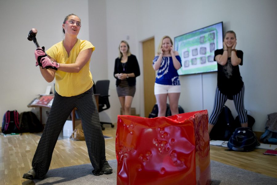 With a leaden sledgehammer, earplugs, and safety glasses, Visiting Assistant Professor of Dance Julie Fox bludgeons a cherry red steel sculpture, part of a new site-specific performance piece unveiled by the internationally recognized multimedia artist Kate Gilmore '97 at the Bates Museum of Art.
.
Gilmore is an artist who synthesizes multiple mediums including performance, video, sculpture, and painting. "Kate Gilmore: In Your Way" features 10 works—nine performance-based videos and one live performance/sculptural installation. Gilmore’s videos focus on herself or several women, wearing stereotypical feminine clothing and footwear while persistently performing difficult, labor-intensive tasks within self-constructed spaces.
.
The performance/sculpture commissioned by the museum for this exhibition consists of five red and pink enamel painted metal cubes, set atop gray carpets. Between one and two p.m. each day, audience members are invited to whack the cubes with a sledge hammer, transforming the minimal forms into expressive sculptures during the course of the exhibition.
.
Fox visited the museum today with students in her first-year seminar, "FYS 437. What is Performance?" She and the students took turns with the sledgehammer and than sat down to discuss art, power, and performance with Gilmore and Stamatina Gregory, curator and art historian. With a leaden sledgehammer, earplugs, and safety glasses, Visiting Assistant Professor of Dance Julie Fox bludgeons a cherry red steel sculpture, part of a new site-specific performance piece unveiled by the internationally recognized multimedia artist Kate Gilmore '97 at the Bates Museum of Art.