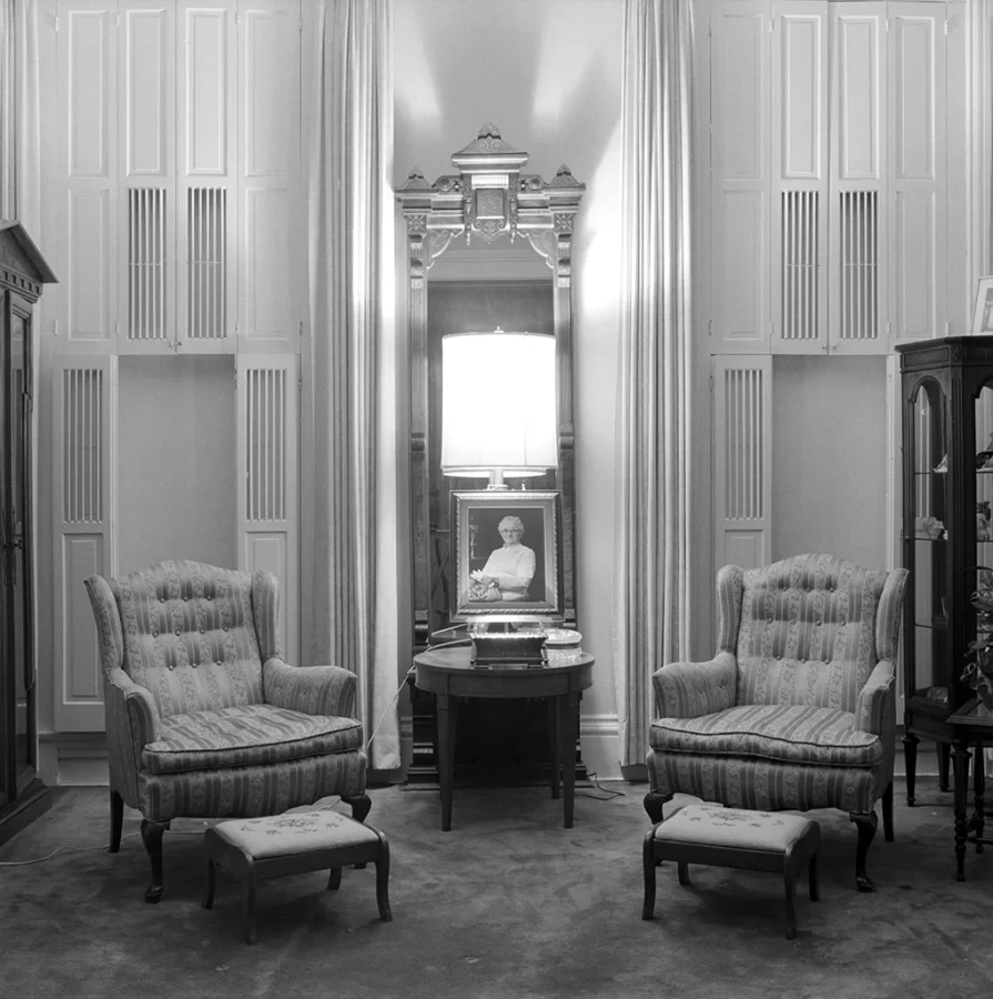Black and white photograph of two tufted chairs flanking the portrait of an elderly woman