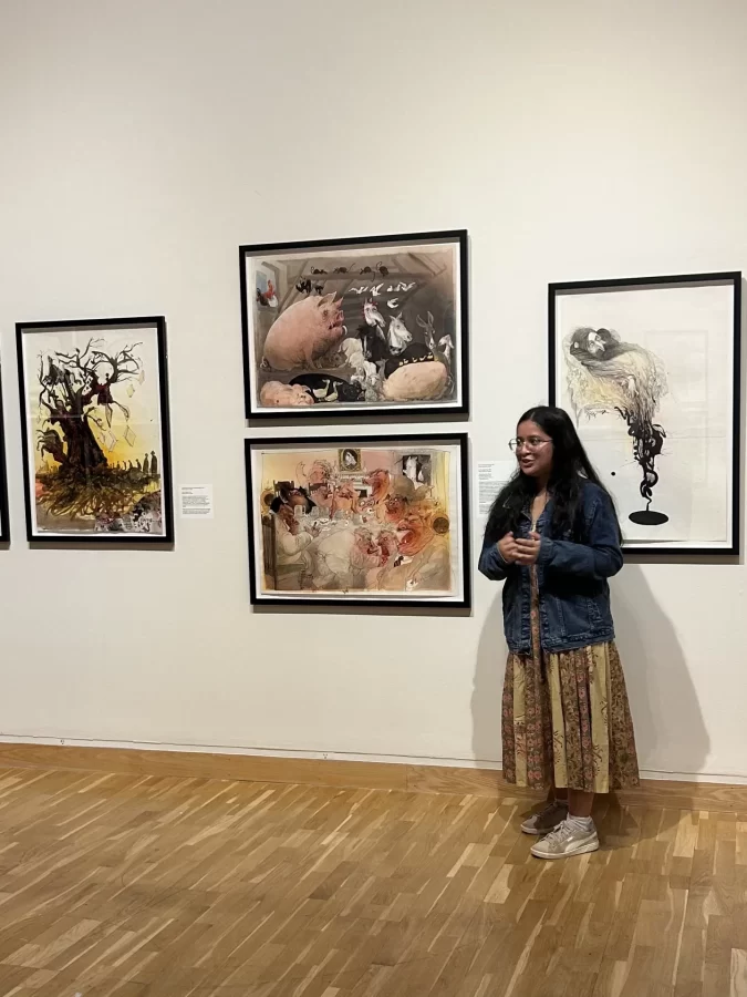 Intern Iffat Ikram ‘28 stands in front of four Ralph Steadman Illustrations