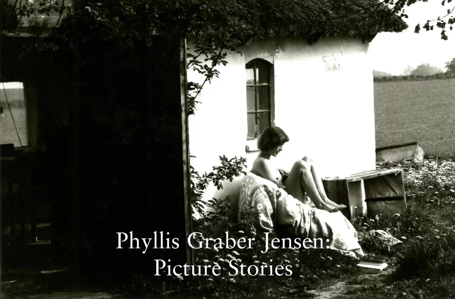 Title Image for Phyllis Graber Jensen: Picture Stories. A young woman sits outside a building with white walls and a thatched roof