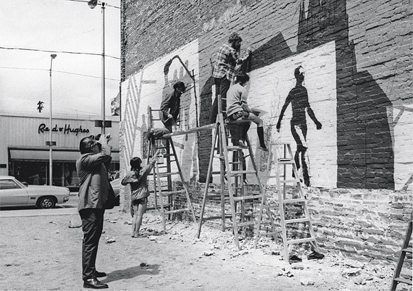 Students paint the Lisbon Street mural in 1971 as an unidentified man films the work.