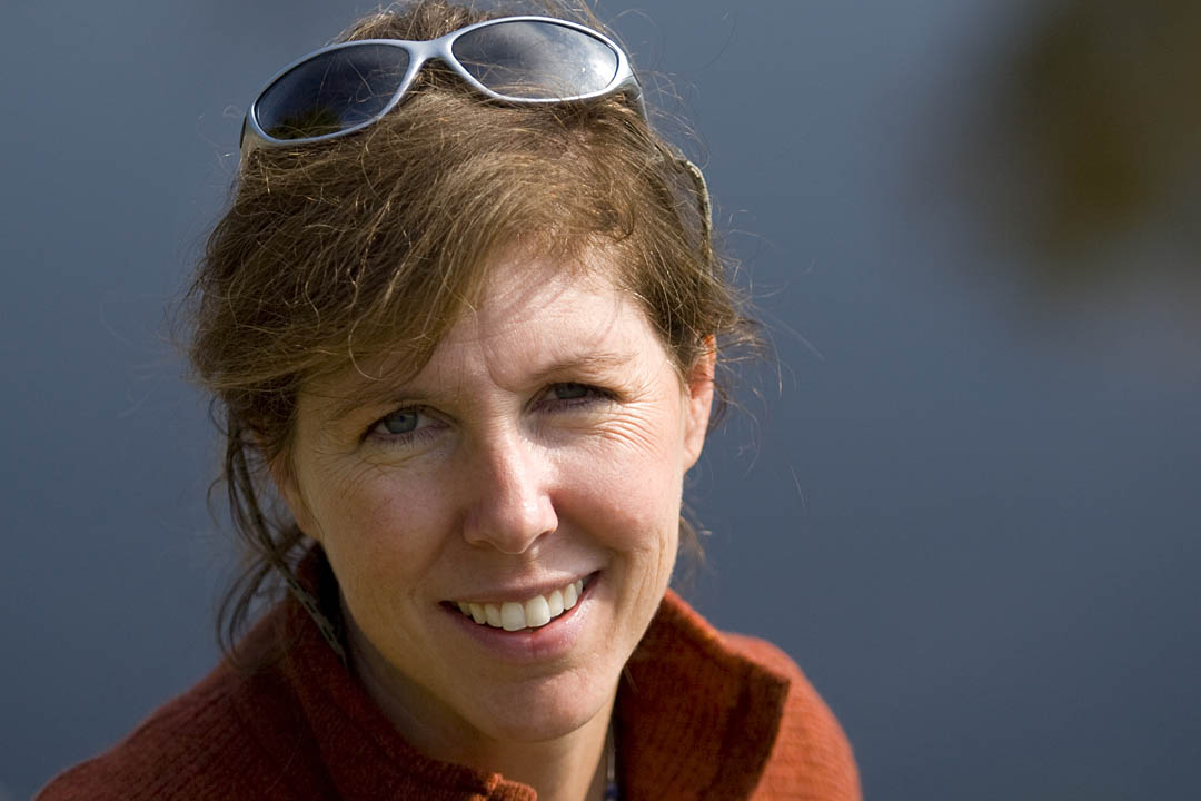 Bates environmental economist Lynne Lewis, associate professor of economics, poses on the Auburn banks of the Androscoggin River behind The Hilton Garden Inn Auburn Riverwatch. Photograph by Phyllis Graber Jensen/Bates College.