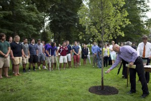 Head football coach Mark Harriman pours water from Lake Andrews on a tree planted at a post-Convocation memorial service for members of the Bates community who died in the previous year . Troy Pappas '16, a freshman on Harriman's team, died in October 2012. (Phyllis Graber Jensen/Bates College)