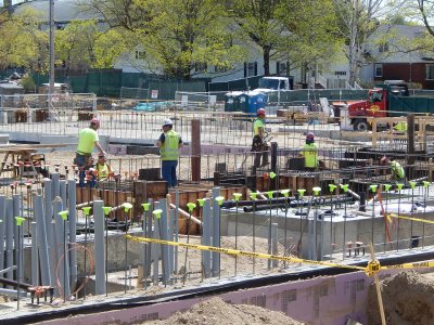 With gray conduits for electrical, telecom and data service in the foreground, workers build a form for concrete footings at 55 Campus Ave. on May 7, 2015. (Doug Hubley/Bates College)