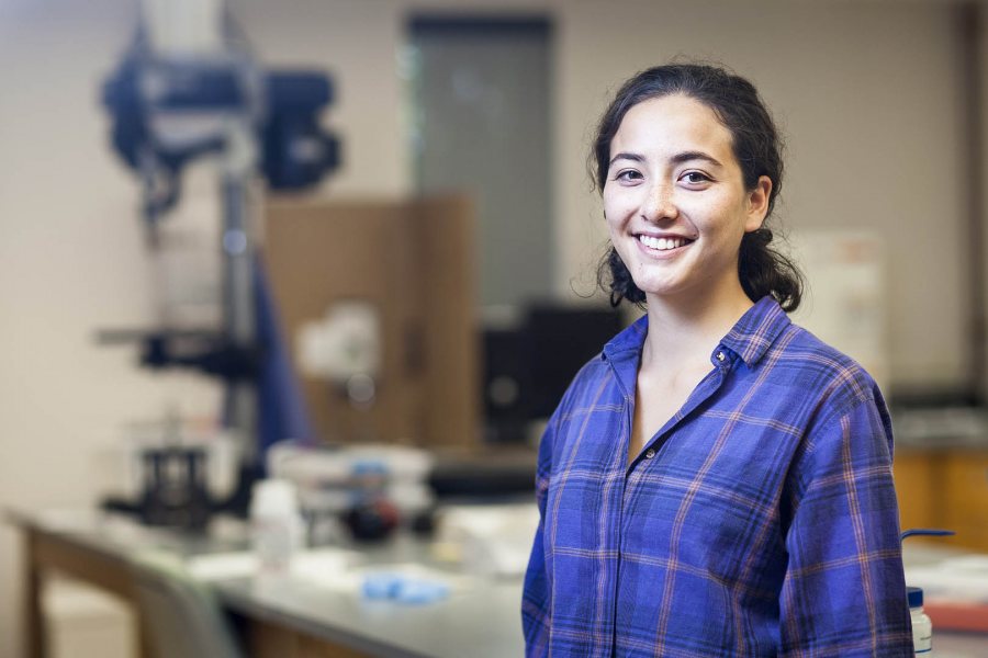 With the drill press that she uses to take cores from slabs of glass in the background, Paige Guevarra '18 of Brooklyn, N.Y., is shown in Genevieve Robert's geology lab. (Josh Kuckens/Bates College)