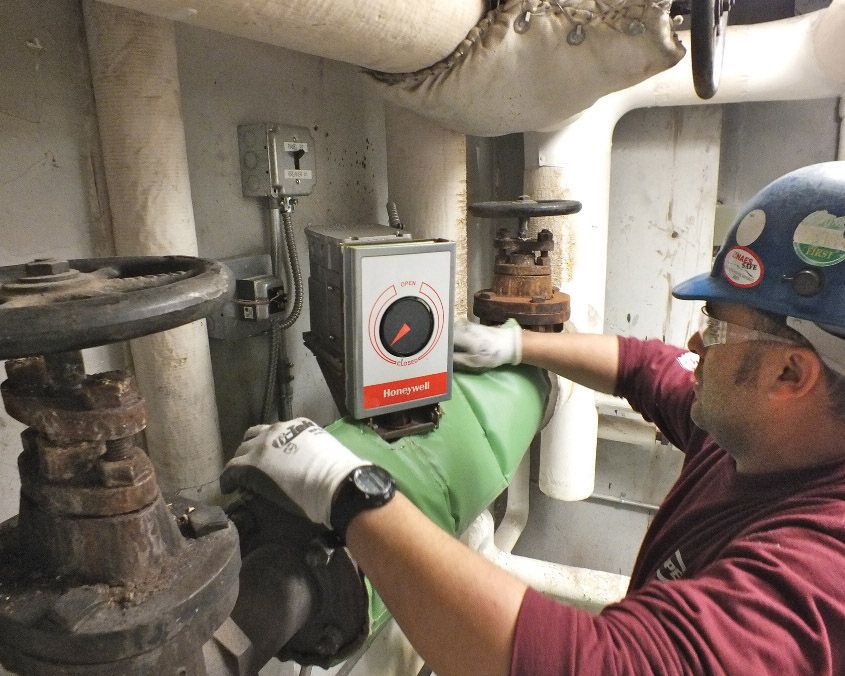 A worker installs Cut'nWrap modular and removable insulating product on a hot-pipe components in a Bates mechanical room. (Photo courtesy of Auburn Manufacturing Co.)