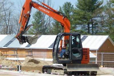 With the old boathouse in the background, an excavator moves dirt at the foundation site of the new boathouse. (Doug Hubley/Bates College) 