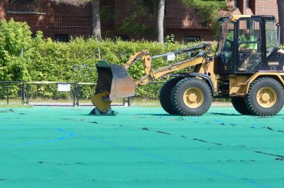 Like a giant pizza cutter, the circular blade on this front-end loader is slicing the Campus Avenue Field AstroTurf on July 6, 2016, prior to rolling it up for removal. (Doug Hubley/Bates College) 