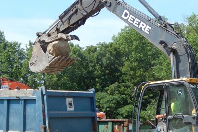 Walter Davenport and his Deere excavator load the broken-up remains of large rocks that had posed something of a problem on the site of Bates' new boathouse. (Doug Hubley/Bates College) 