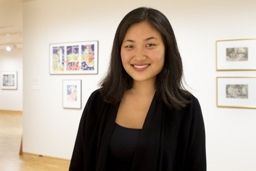 Lillie Shulman '17 of Brooklyn is shown amidst the Bates Museum of Art exhibition Mythology, which she helped curate. Hanging behind her are watercolors by Wally Reinhardt. (Phyllis Graber Jensen/Bates College)