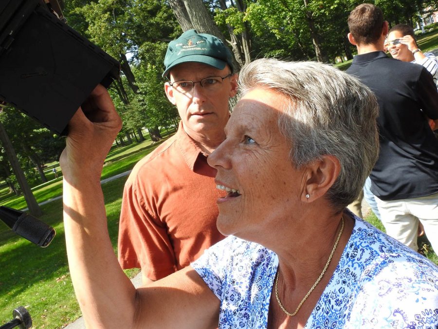 Georgette Dumais, an academic administrative assistant, views the eclipse through an old Speed Graphic camera belonging to Associate Professor of Chemisty Matt Côté, who looks on. (Jay Burns/Bates College)