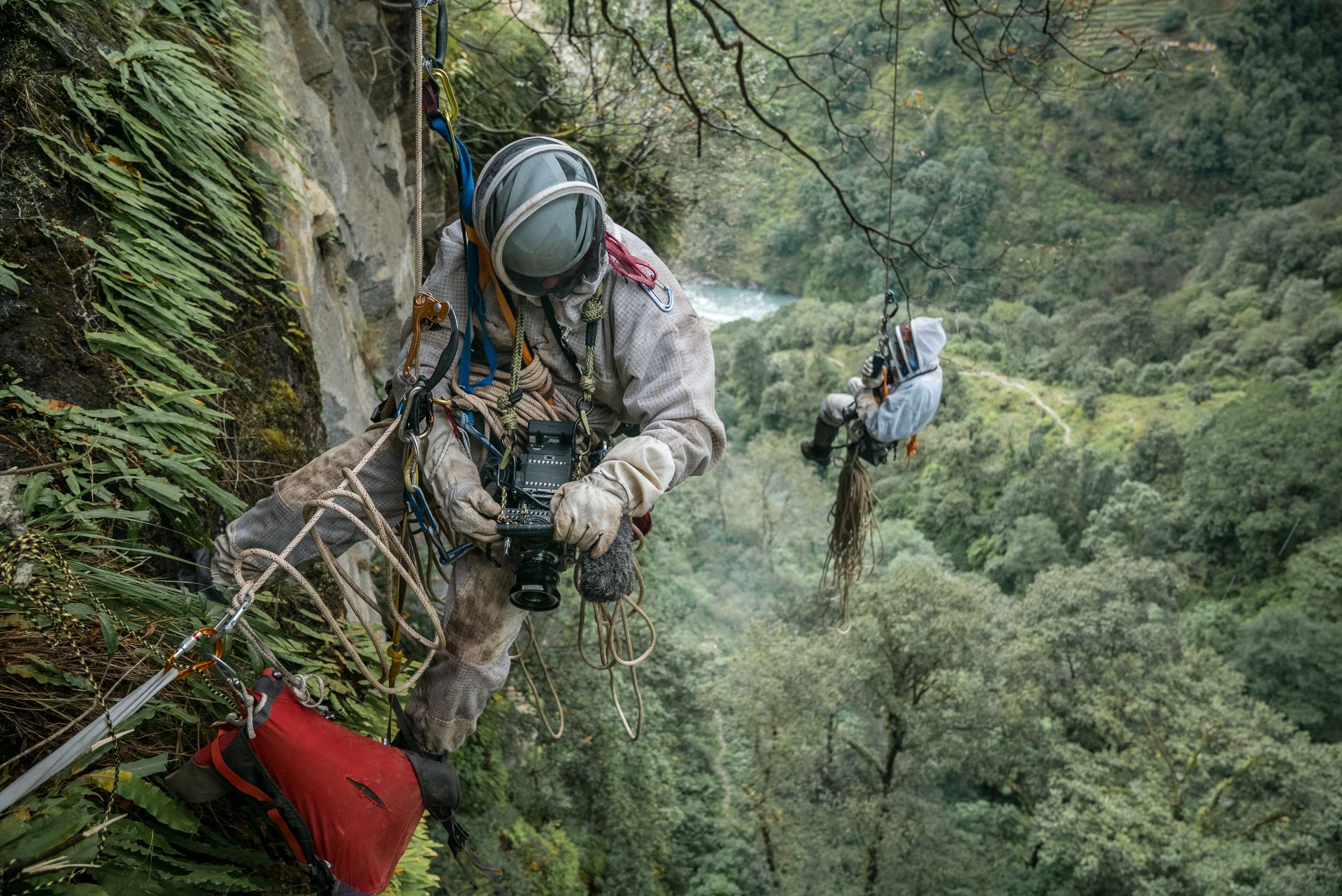 Wearing bee suits, Renan Ozturk and Ben Ayers ’99 prepare to capture Mauli Dhan Rai as he harvests a valuable hallucinogenic honey from a cliffside in Nepal's Hongu River Valley. (Courtesy of Renan Ozturk)