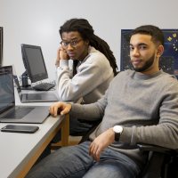 Physics students Kingdell S. Valdez ‘19 of Andover, Mass. (gray sweater) and Cristopher Thompson '19 of Macon, Ga., (Bates track sweatshirt) pose for photographs and discuss a physics problem at the blackboard in third-floor Carnegie Science physics lab on March 7, 2019.They are working on a collaborative physics senior project, doing different aspects w/similar data, turning in separate documents.