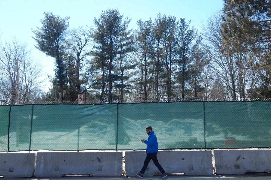 A student passes the newly fenced-in site of Bates' future science building on March 19, 2019. (Doug Hubley/Bates College)