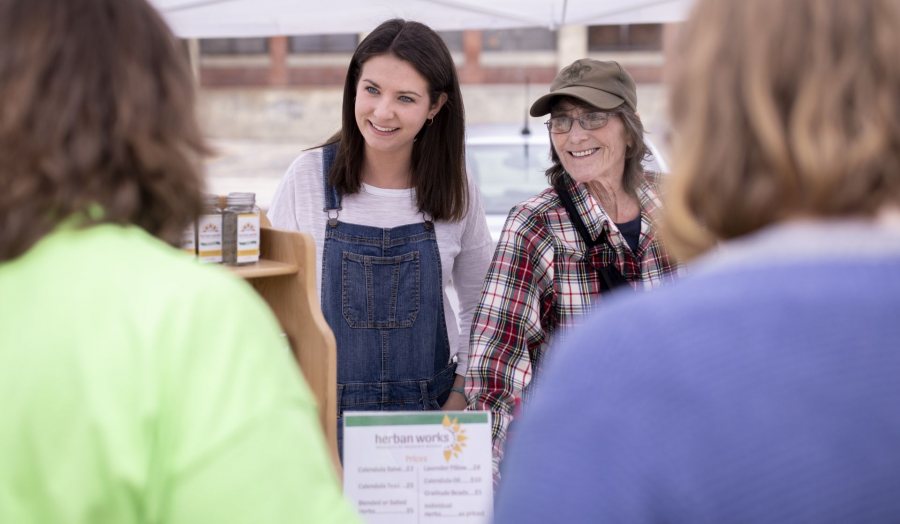 Clio Barr '19 of Hallowell, Maine, is a STA/RT (SHORT TERM ACTION/RESEARCH TEAM) partner with the Center for Wisdom's Women Herban Works. Her project title is Creating Marketing Materials and a Business Plan for Sophia's House.On the first spring day of the 2019 Lewiston Farmer's Market, Barr sells products on Sunday, May 12, with Judy Maloneygarden and production coordinator and volunteer Mary Hopkins, who also helps with harvesting and planting.