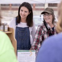 Clio Barr is a STA/RT (SHORT TERM ACTION/RESEARCH TEAM) partner with the Center for Wisdom's Women Herban Works. Her project title is Creating Marketing Materials and a Business Plan for Sophia's House.On the first spring day of the 2019 Lewiston Farmer's Market, Barr sells products on Sunday, May 12, with Judy Maloneygarden and production coordinator and volunteer Mary Hopkins, who also helps with harvesting and planting.