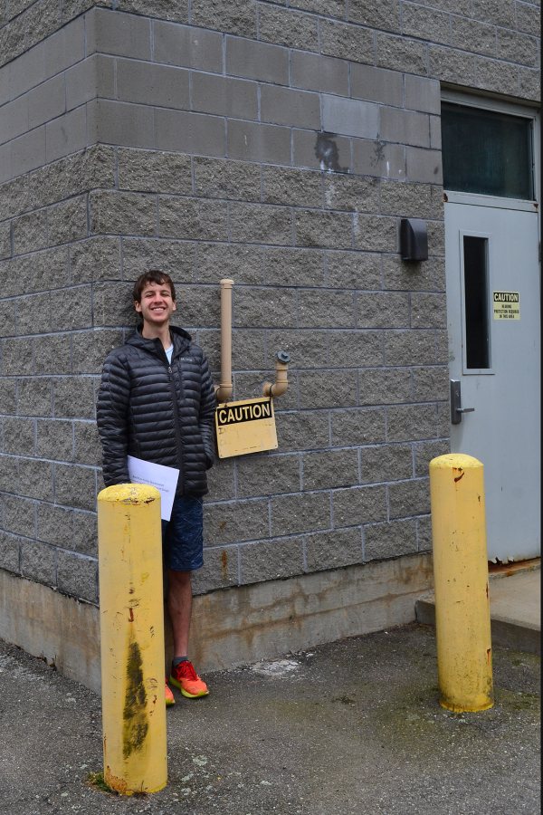 A member of the “In Search of Higher Ground” class, Henry Colt ’19 poses at the wastewater treatment plant by the sea in Boothbay Harbor, Maine. Six feet tall, Colt marks the level sea water could reach during a northeaster in the year 2060 according to one scenario. (Lynne Lewis/Bates College)