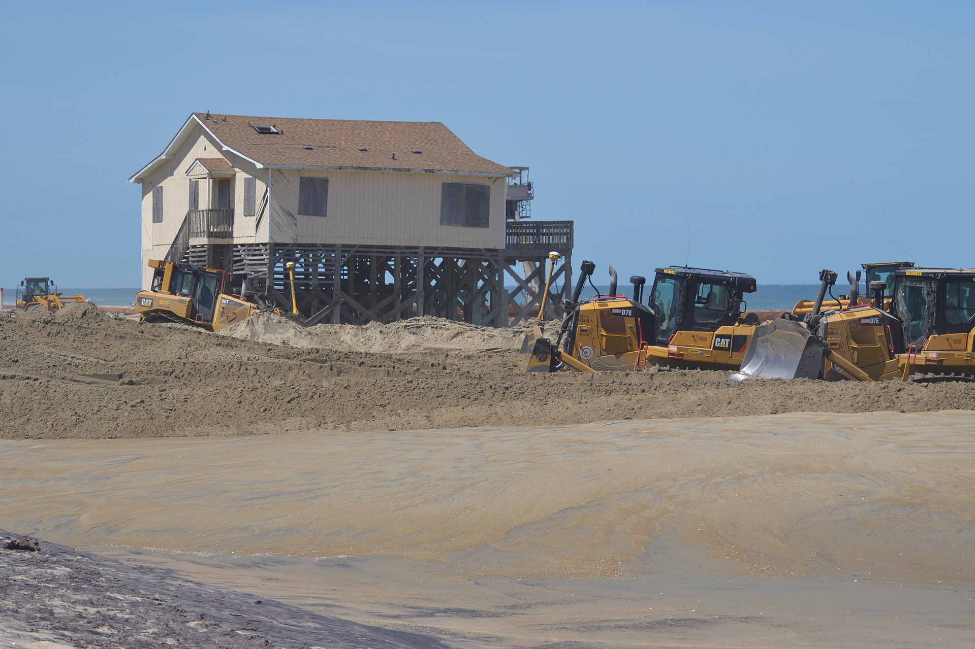 Bulldozers spread sand near a beach house at Nags Head, N.C., part of a $43 million beach “renourishment” project. Sand is dredged from the ocean floor and pumped more than a mile from an offshore “borrow” site to the beach. (Lynne Lewis for Bates College)