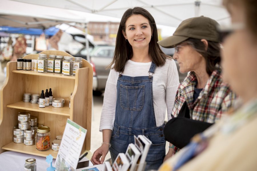 Clio Barr '19 of Hallowell, Maine, is a STA/RT (SHORT TERM ACTION/RESEARCH TEAM) partner with the Center for Wisdom's Women Herban Works. Her project title is Creating Marketing Materials and a Business Plan for Sophia's House.On the first spring day of the 2019 Lewiston Farmer's Market, Barr sells products on Sunday, May 12, with Judy Maloney garden and production coordinator and volunteer Mary Hopkins, who also helps with harvesting and planting.