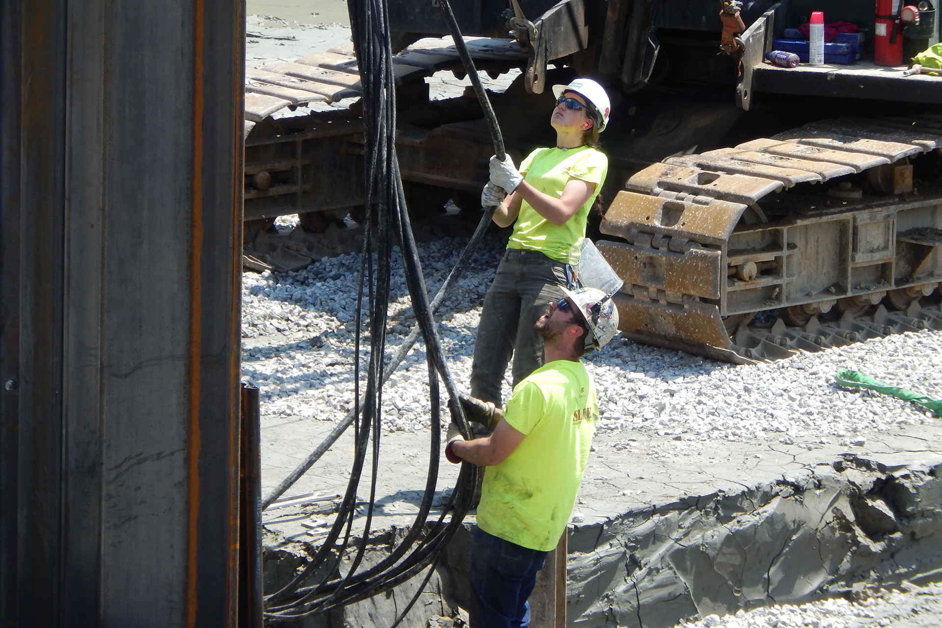 Two H.B. Fleming employees guide the vibro hammer into position atop the sheet pile at left. They're pulling hoses that connect the hammer to its power unit. (Doug Hubley/Bates College)