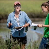 Professor of Geology Beverly Johnson uses a sediment elevation table to measure the height of the Sprague River Salt Marsh, part of the Bates–Morse Mountain Conservation Area..These data are used to measure the response of the marsh to rising sea level and storm activity, Johnson says. Four years ago, she and her Short Term geology students traveled to the Sprague, where they placed rods deep in the marsh as benchmarks to measure future changes.Show with Laura Sewall (in garnet baseball cap), Harward Center for Community Partnerships, Director of Bates Morse Mountain Conservation Area, and Vanessa Paolella '21 of Dingmen's Ferry, Pa., who has been working with Johnson on geology research over the summer.Also present: Clailre Enterline (in green shirt and blue baseball cap), Research Coordinator with the Maine Coastal Program. And (not in selects but wearing a blue baseball cap and blue shirt) Ellen Bartow-Gieelie, Coastal Fellow with the Maine Coastal Program.