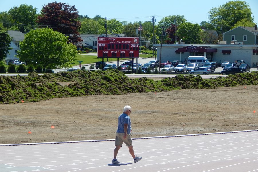 With a walker on the Russell Street track in the foreground, heaps of old sod on the Bates soccer field are awaiting removal on on June 12. (Doug Hubley/Bates College)