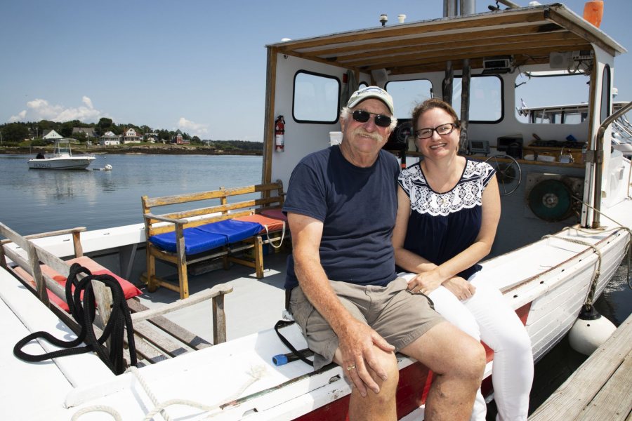 Kate McGowen Wing, '01, and her father Captain Jay McGowen, West Wind Lobster Tours in Bailey Island, pose for a portrait in between tours on July 26, 2019. Captain Jay leads a sports fishing tour in the morning and switches over to lobster tours in the afternoon, during this transition, his daughter Kate McGowen Wing brought him a sandwich for lunch. Kate works behind the scenes helping her father organize and manage all of the tourism.