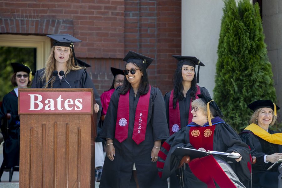 Senior Gift co-chair Erika Lamere ’19 speaks to the Commencement audience, joined on the platform by co-chairs Elizah Laurenceau ’19 and Taylor Lough ’19. Seated are President Clayton Spencer and Commencement speaker Jennifer Doudna. (Phyllis Graber Jensen/Bates College)